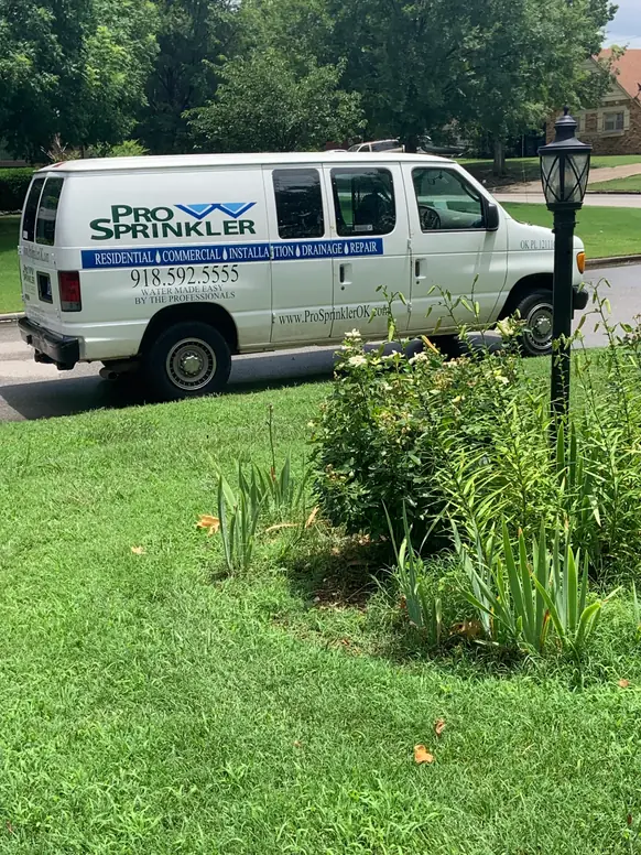 The Pro Sprinkler van parked at the curb of a Tulsa street, green wordmark and blue chevron on the side panel
